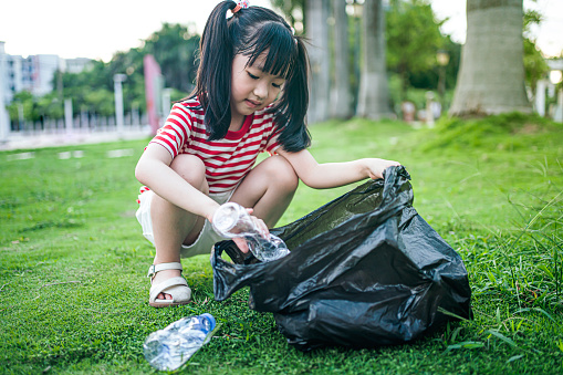 The girl picked up the beverage bottle on the ground and put it into the garbage bag，Environmental protection theme, caring for nature theme