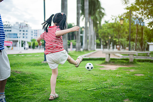 An Asian girl is playing football in the park