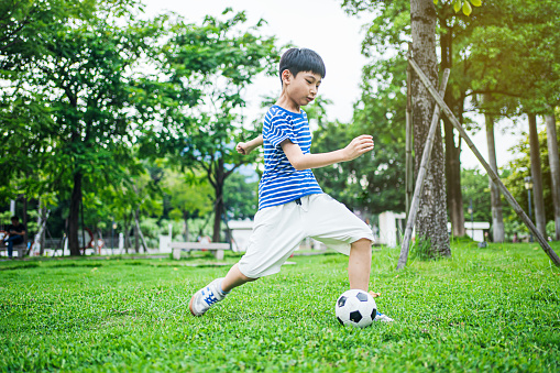 An Asian boy is playing football in the park