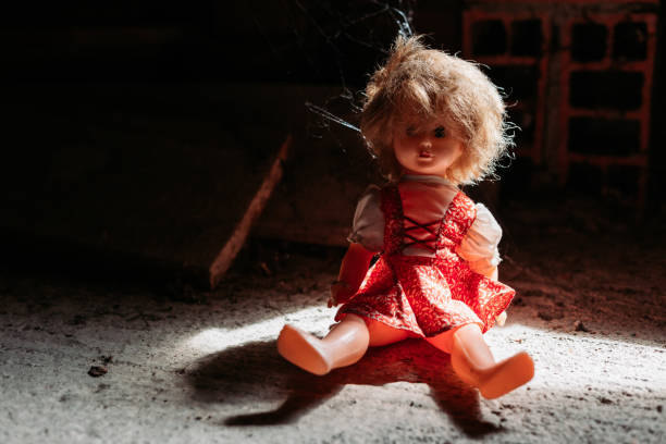 Old doll sitting on dirty ground. Scary look, Halloween concept