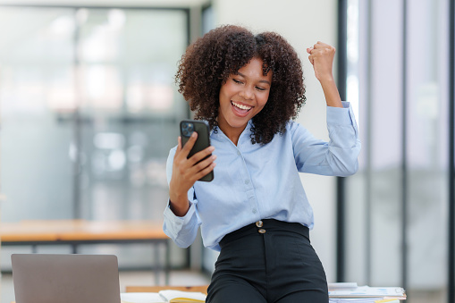 Beautiful business woman using smartphone is delighted and excited by the success she has achieved through her office cell phone.