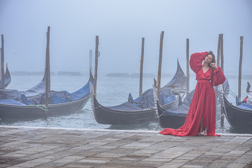Venice, Italy - 15 Nov, 2022: A young woman in a red dress poses for a portrait along the Grand Canal