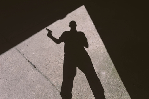 Shadow of a man holding gun in building doorway. Actor performance, not real life