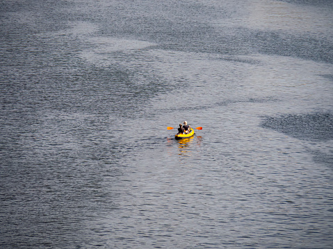 Rear view of a couple kayaking in a river in Bilbao city. Water recreation activity for summertime. Yellow kayak in the middle of an estuary as background with copy space.