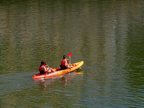 Bilbao, Spain - August 19th, 2023: Two unrecognizable girls kayaking in the Nervion river in Bilbao city estuary. Water summer activity for city vacations. Friends in a boat on a river rowing.