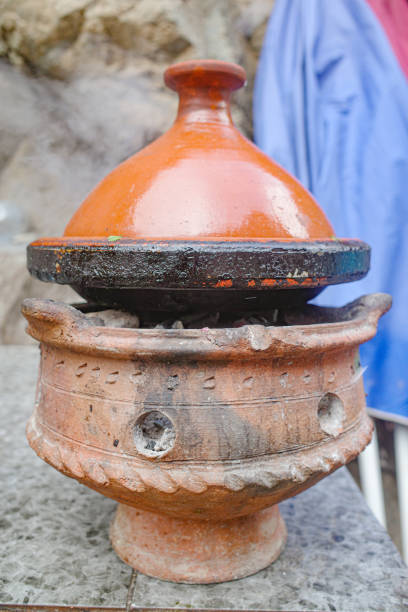 Morocco, Ait Benhaddou, November 16, 2025: Close-up of a traditional meat tajine served in an earthenware dish, topped with tomato slices and almonds on a wooden table, with bread, mint tea pot, water bottle and colorful decor of a cozy restaurant softly blurred in the background.