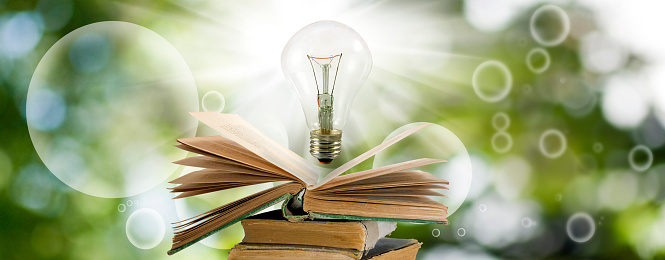 The image of a light bulb over an open book is a symbol of the concept of knowledge, learning and inspiration. Light bulb and open book on green blurred background