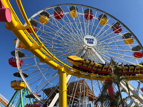 Low-angle shot of people riding the rollercoaster in front of the ferris wheel at Santa Monica Pier, California