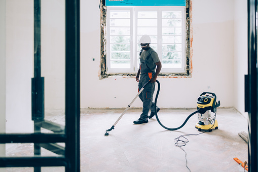 An African American construction worker vacuuming the floors while renovating an apartment.