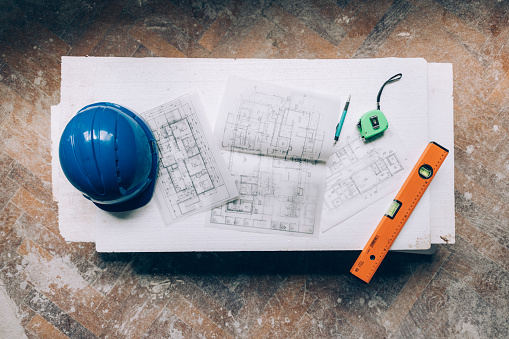 An overhead shot of construction tools, blueprints and a blue helmet.