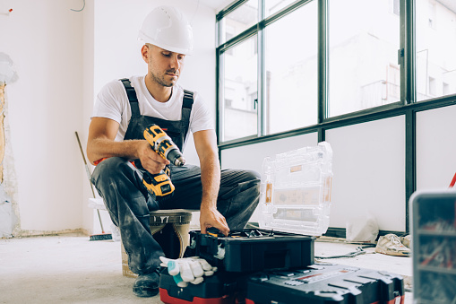 A white construction worker renovating an apartment using various tools.