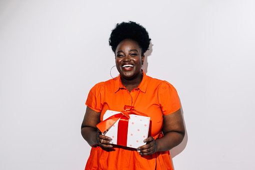 A portrait of a happy African American woman wearing an orange dress and holding a birthday present.