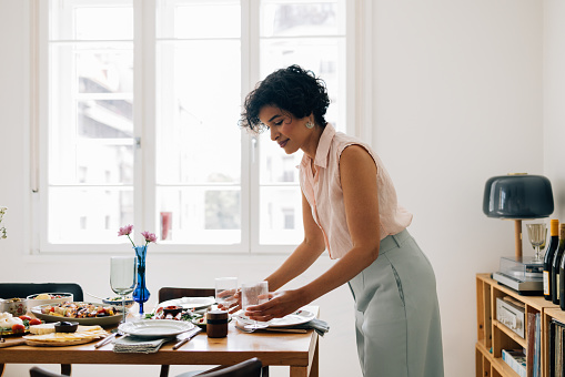 A smiling Latin American woman setting the dining table for lunch.