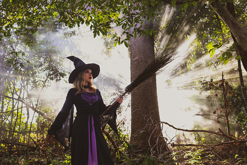 Portrait Witch holds the magic broom in the rustic  forest on Halloween day