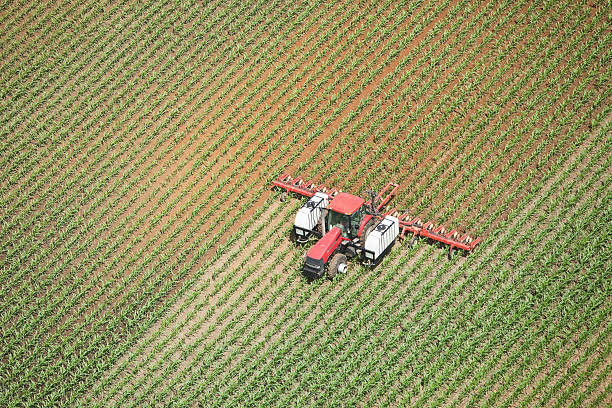 Tractor Applying Liquid Nitrogen Fertilizer to Corn Field Aerial view of a tractor towing an applicator is spraying liquid nitrogen fertilizer on a late Spring corn field. The left field and behind the spreader is wet with darker soil. Shot from the open window of a small plane. http://www.banksphotos.com/LightboxBanners/Aerial.jpg http://www.banksphotos.com/LightboxBanners/AgFarming.jpg nitrogen stock pictures, royalty-free photos & images