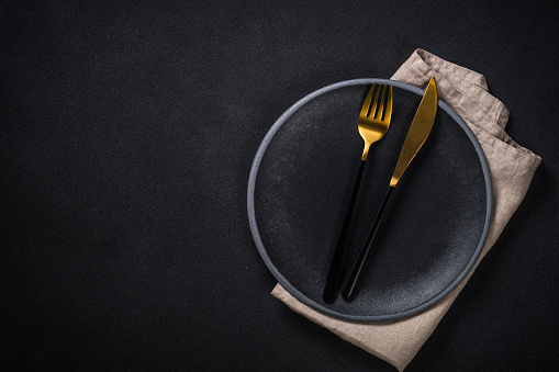 Black plate with luxury cutlery at black stone background. Top view with copy space.