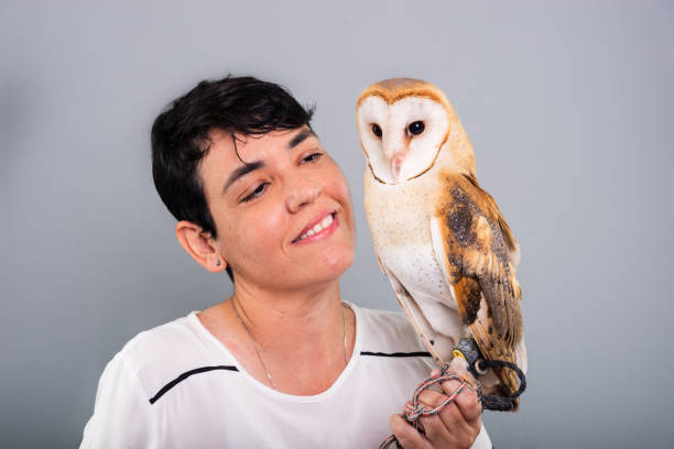 A woman lovingly looking at her owl. Wild animal. Against gray background.