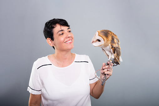A woman lovingly looking at her owl. Wild animal. Against gray background.