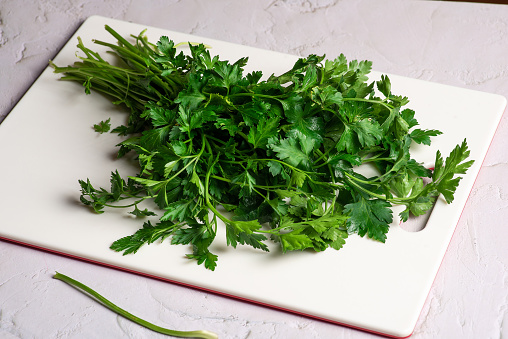 Fresh, green parsley leaves on a white, plastic kitchen chopping board
