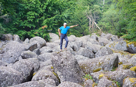 A man balancing on a big rock on a rocky river .