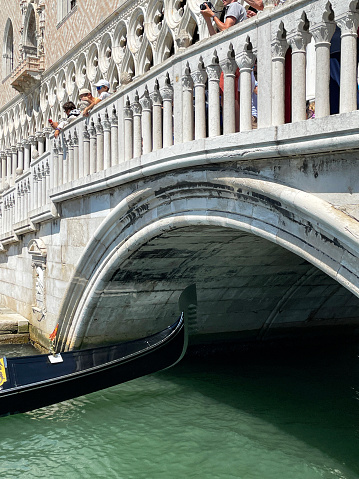 Grand Canal, Venice, Italy - July 14, 2023: Stock photo showing close-up view of the Rialto Bridge (Ponte di Rialto) spanning the Grand Canal, with gondola boat being piloted under bridge arch.