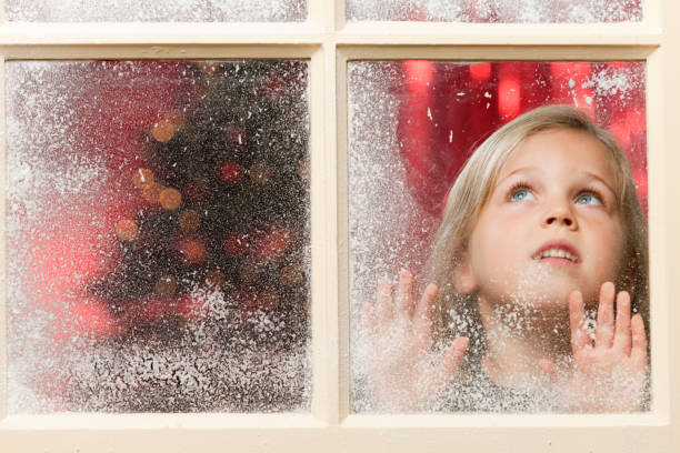 istock girl looking through snowy window at Christmas 165771577