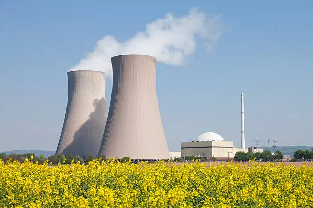 Nuclear power station with steaming cooling towers and blooming canola field. Location: Lower Saxony, Germany.