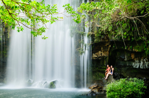 Two women relaxing next to a waterfall.  Llanos de Cortes Waterfall in Bagaces, Guanacaste, Costa Rica