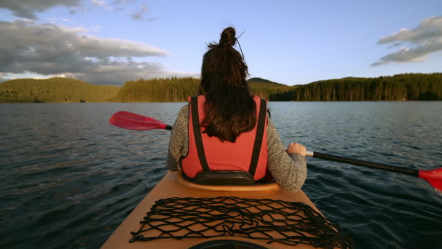 Woman kayaking on sunset in mountain lake.