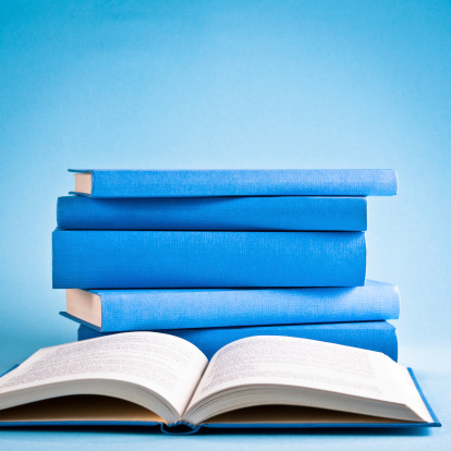 Opened book against stack of books isolated on blue background. Square composition, copy space, studio shot.