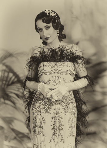 Portrait sexy woman in twenties old style beautiful face professional makeup retro dress ostrich feather boa cold wave hairstyle. Classic sepia black and white vintage photo. Roar 1920s fashion model.