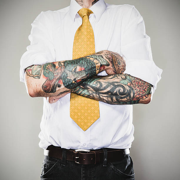 New Professional A business man stands with his tattooed arms folded across his white collared shirt and tie.  Two forearm sleeve tattoos.  Representing a new generation of modern business standards and style. forearm tattoos men stock pictures, royalty-free photos & images