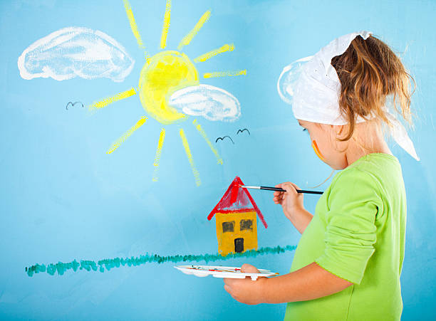 Four years old female artist drawing little house on blue background.