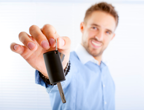 Young happy car selling manager giving car keys to client