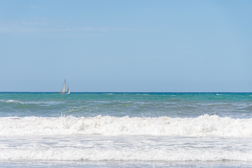 Breaking waves on the seashore and a sailboat in the background.