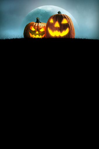Two illuminated jack o'lanterns rest on a grassy hill in front of a rising full moon.