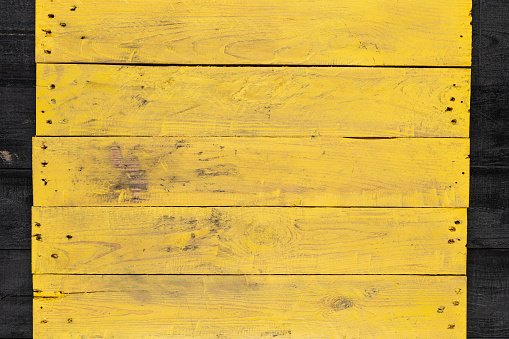 Weathered yellow wood texture background. Yellow stained wooden billboard close-up. Horizontal direction boards. Wavy pattern of wood fibers.