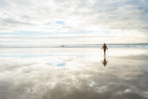 Girl walking on the Moonlight Beach, in San Diego, California, on a cloudy day. The scene is magical. The clouds are reflected from the sky, and scene of the girl looks like she is reflecting on the beach and walking on clouds