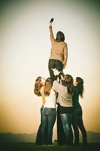 Group of women raising up a friend with a telephone to the sky. Modern communications, cloud computing concept.