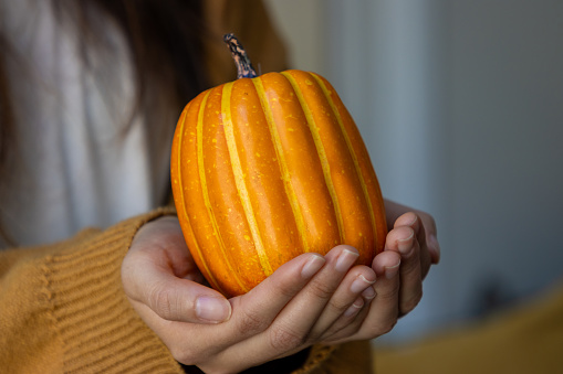 A woman holds a small pumpkin used as decoration in autumn.