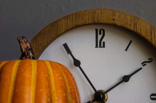 A clock behind a small pumpkin. Concept photo for autumn, Thanksgiving and Halloween.