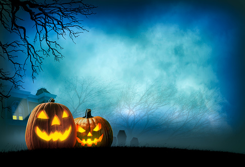Two illuminated jack o'lanterns sit in front of a haunted house in the distance. Bare trees in the fog and mist frame the haunted house.