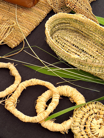 Vertical high angle closeup photo of various items hand woven using Australian native plants on a black cloth background.