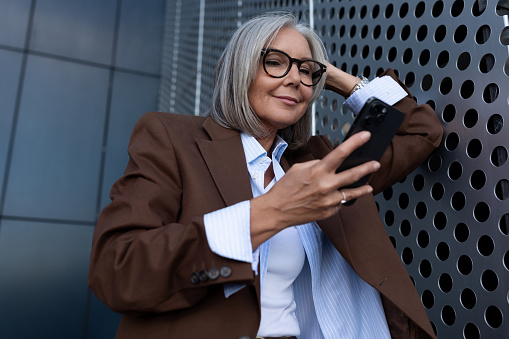 beautiful gray-haired successful mature business woman in glasses dressed in a respectable way chats in a smartphone.