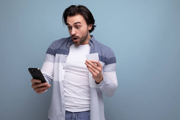 istock surprised young brunette man makes an online purchase using a smartphone and a money card 1658008346