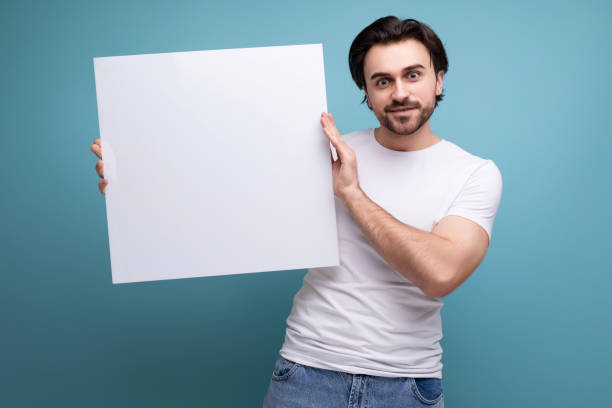 istock cute brutal brunette guy holding a paper sheet with empty space for information 1658009422