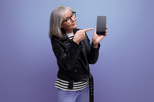 positive modern 60s modern old lady with gray hair holding a phone with a mockup on a bright background with copy space.