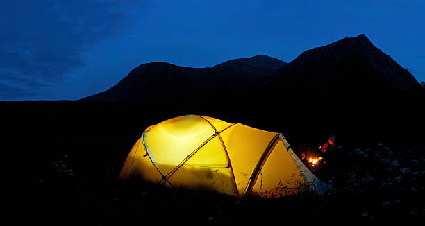 Mountain wilderness camping toasting mallows over camp fire Child toasting marshmallows over open camp fire beside an illuminated yellow dome tent beneath the silhouetted mountain peaks of Glen Coe, Scotland. ProPhoto RGB profile for maximum color fidelity and gamut. glen etive photos stock pictures, royalty-free photos & images