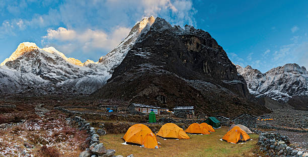 Teahouse camp under Himalaya mountain peaks panorama sunrise First warm rays of daybreak illuminating the snow capped peaks and dramatic rocky pinnacles of Kusum Kanguru (6397m) overlooking the bright yellow dome tents and stone lodges of Thangnak deep in the remote wilderness of the Makalu Barun National Park of Nepal. ProPhoto RGB profile for maximum color fidelity and gamut. base camp stock pictures, royalty-free photos & images