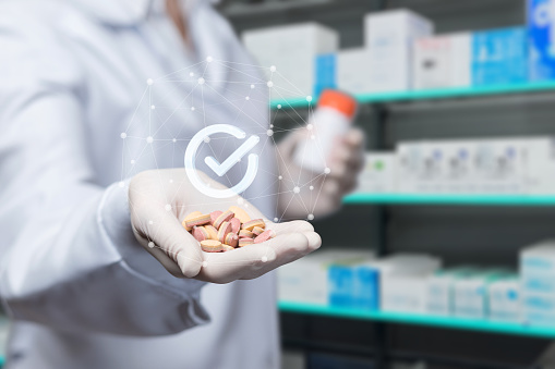 The concept of quality medicines in a pharmacy. The pharmacist shows pills in the background of the pharmacy.